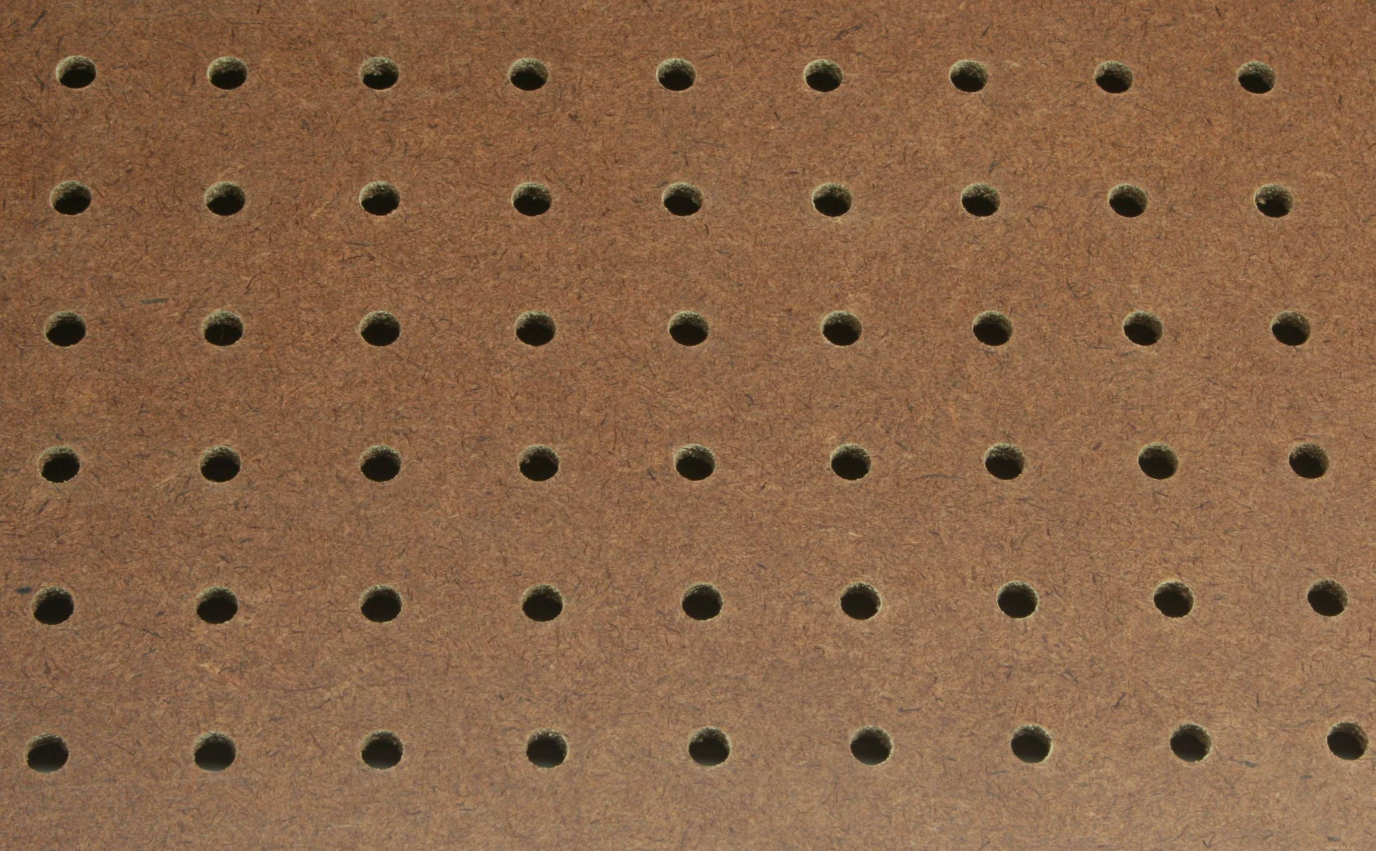 Primer plano de un tablero perforado (pegboard), el sistema típico para colgar herramientas en la pared de un taller